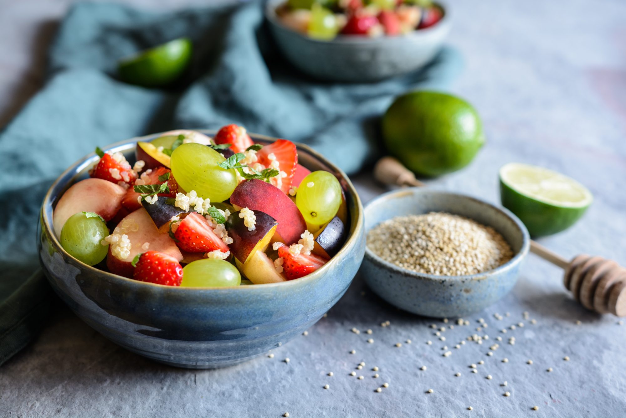 Healthy fruit salad with quinoa, strawberry, peach, white grapes, plums, mint and honey lime dressing